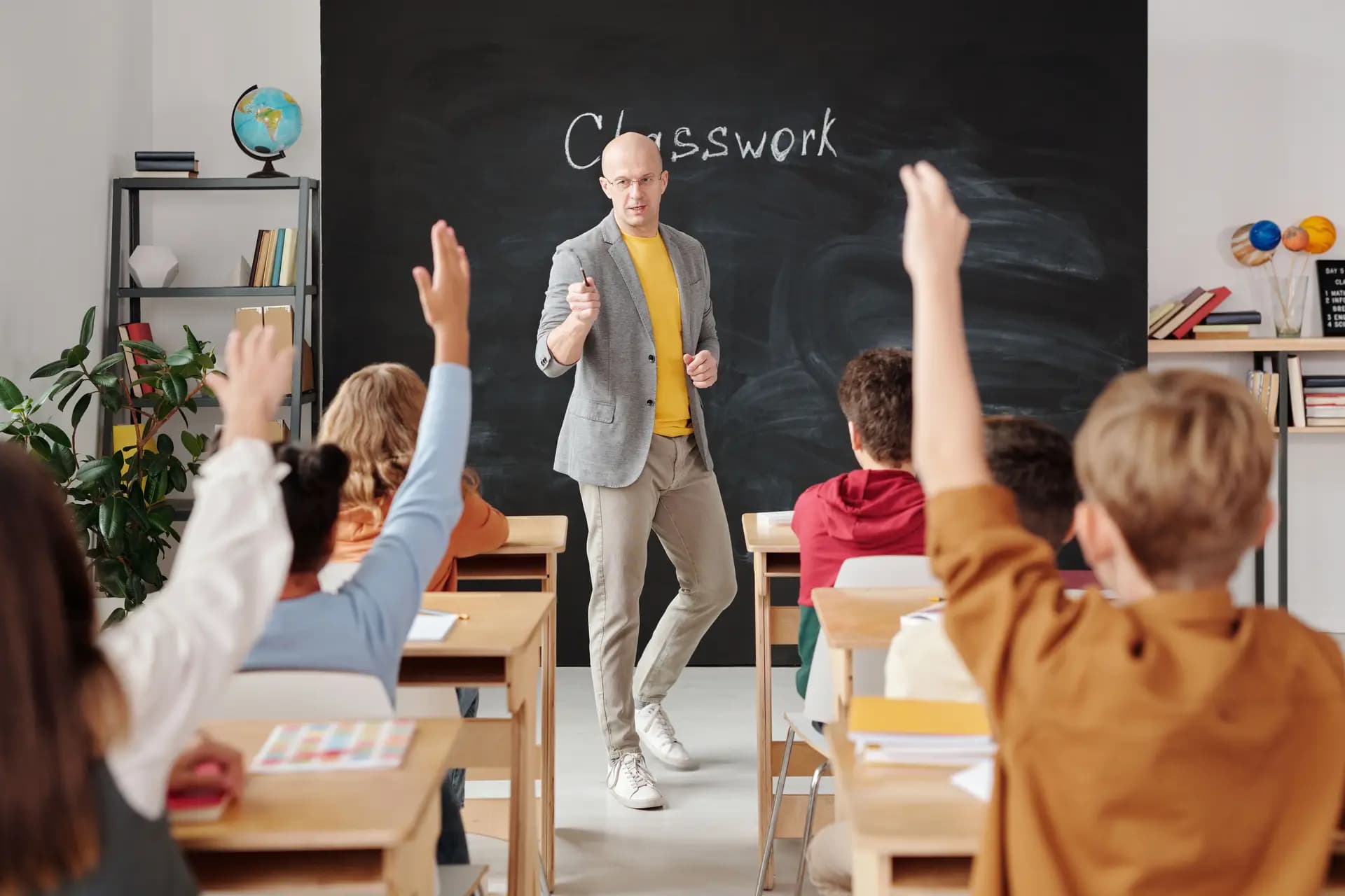 A teacher at the blackboard with students raising their hands
